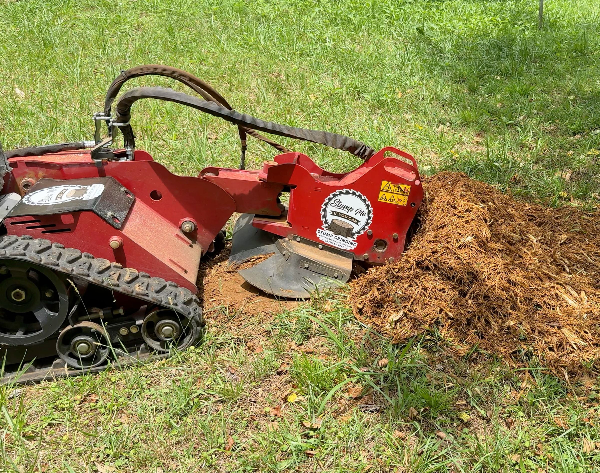 Kevin's red tracked stump grinder, branded with the Stump Me logo, grinding a stump down into a pile of chips